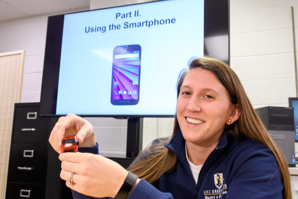 Woman in UNCG sweater smiling in front of TV